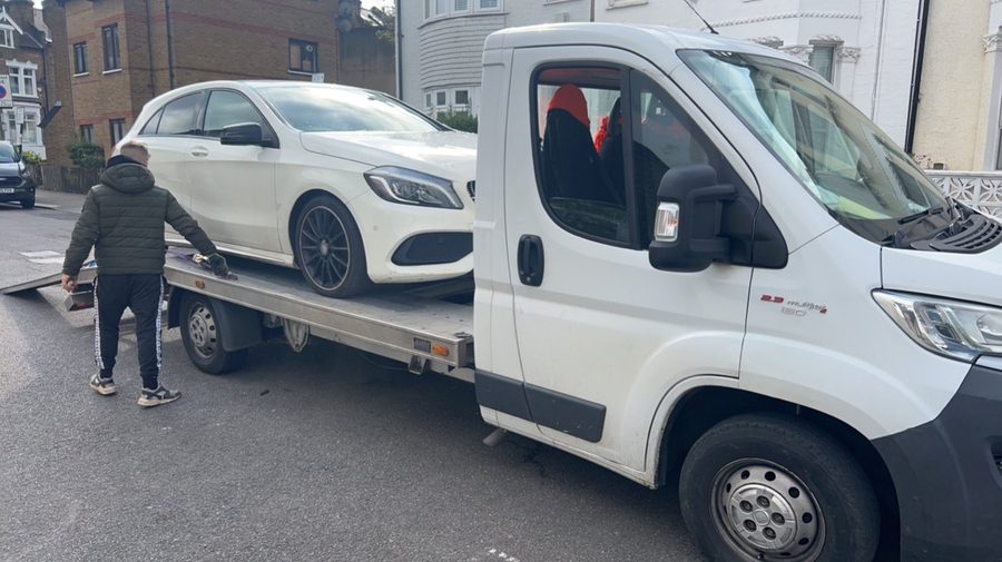 A white Mercedes-Benz A-Class being loaded onto a flatbed transporter on a residential street